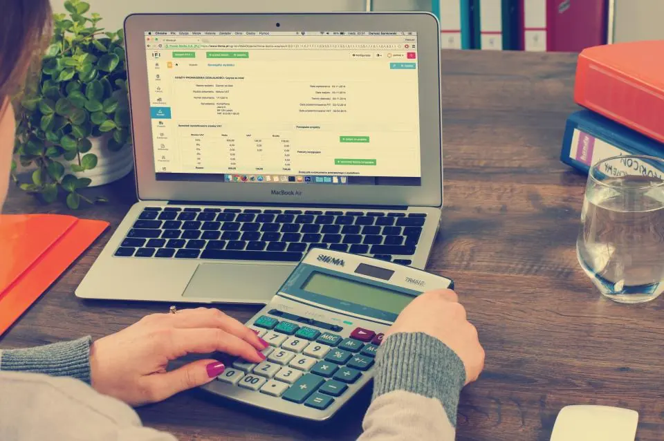 Mains utilisant une calculatrice devant un ordinateur portable